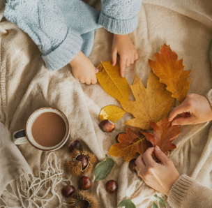 Manos de un niño y un adulto ordenando hojas de otoño y castañas sobre una manta - blog de Clínica Lazos