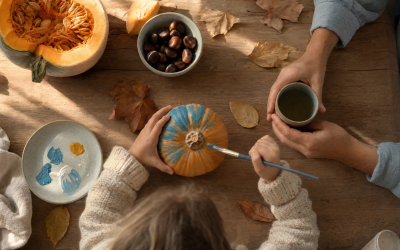 Manos de un niño y un adulto decorando calabazas en una mesa de cocina en otoño - blog de Clínica Lazos